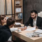 Advogado conversa com clientes enquanto analizam documentos jurídicos em uma mesa de escritório.